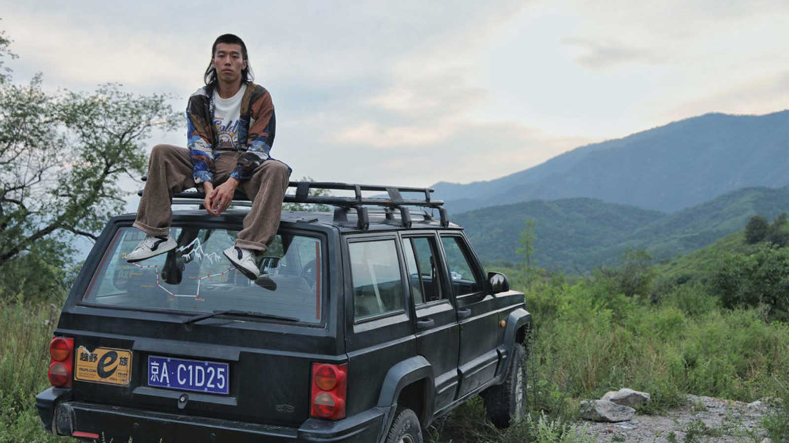 Male character sitting atop Jeep with mountain in background