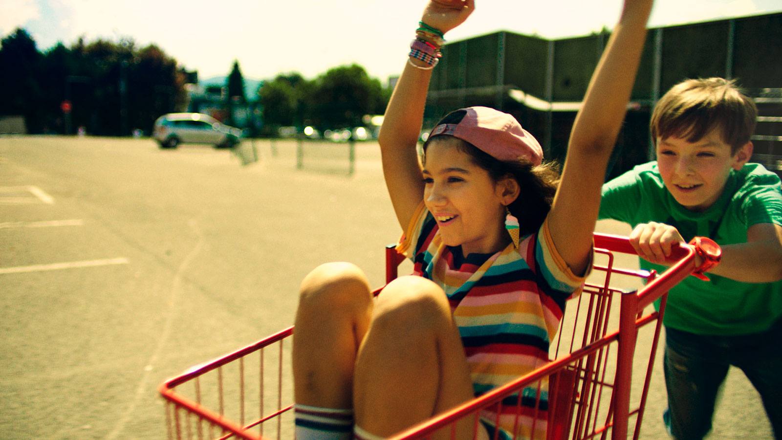 Young boy pushing girl in shopping cart in a parking lot on a bright summer day