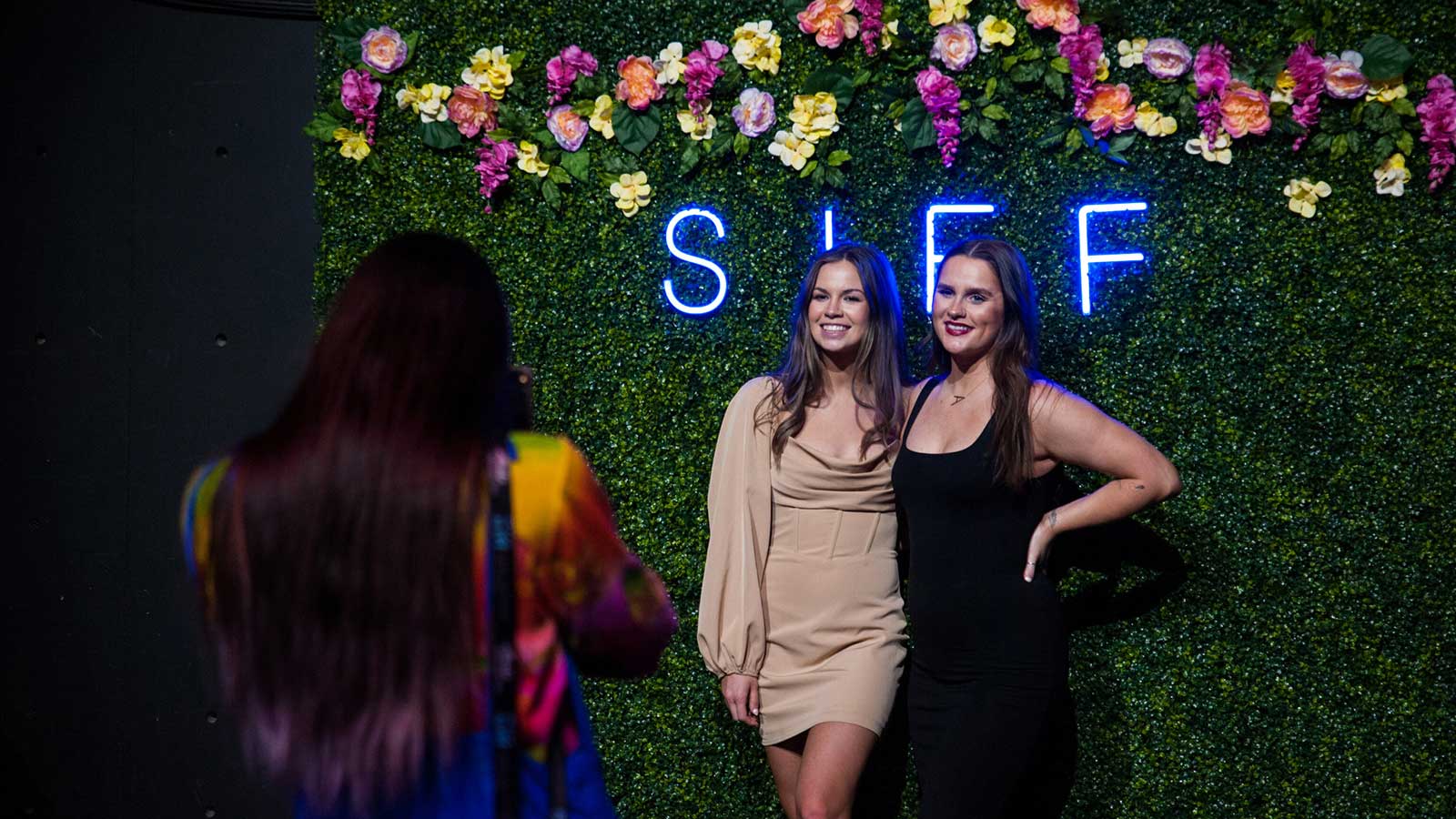 Guests pose in front of a photo op with a SIFF neon sign and colorful flowers